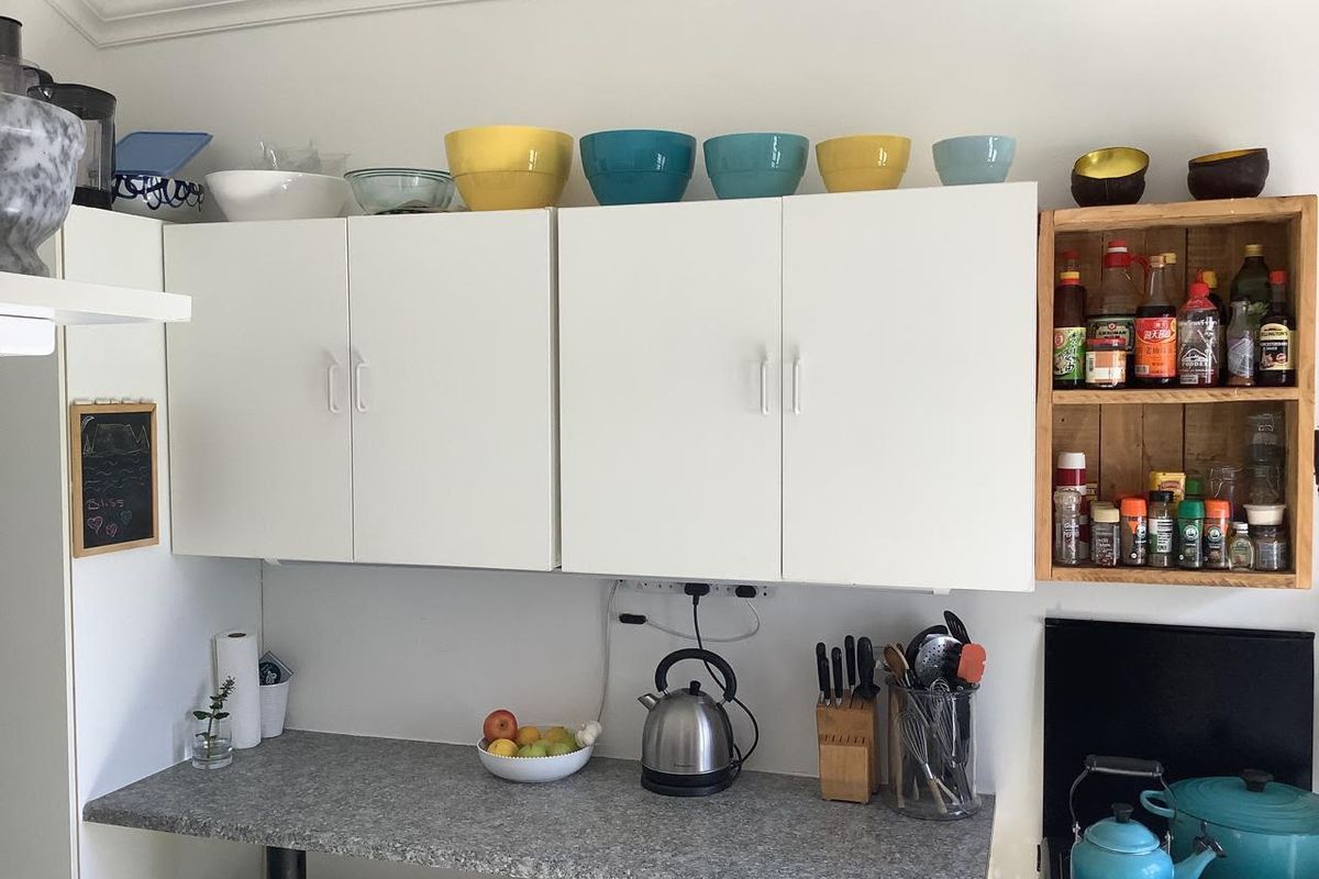 A functional kitchen area featuring white wall-mounted cabinetry, a grey laminate countertop, and open timber shelving for convenient storage.