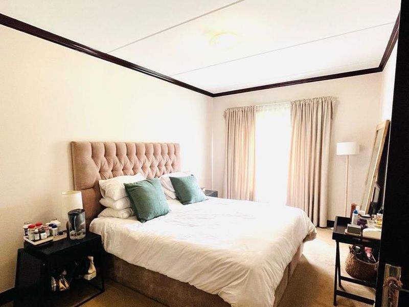 A well-lit bedroom featuring neutral carpeting, dark crown molding, and floor-to-ceiling curtains, providing a comfortable and functional sleeping space.