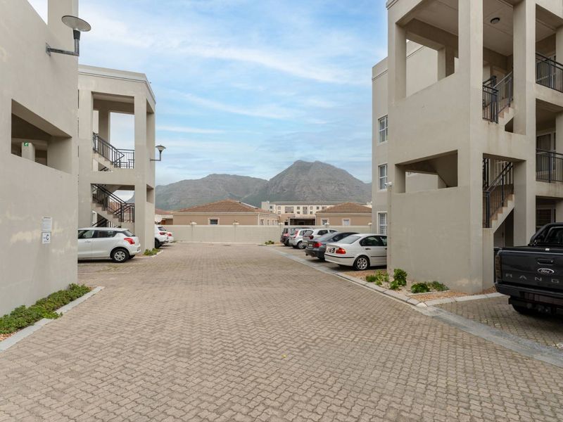 Exterior view of the apartment complex parking area featuring paved driveway, multi-level building facades, and mountain views in the background.