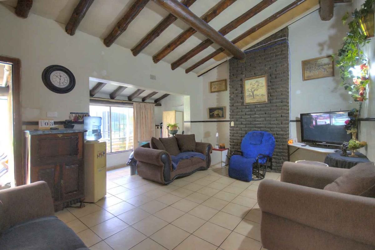 Spacious living room featuring exposed timber ceiling beams, a rustic brick fireplace feature wall, and tiled flooring with access to an outdoor area.