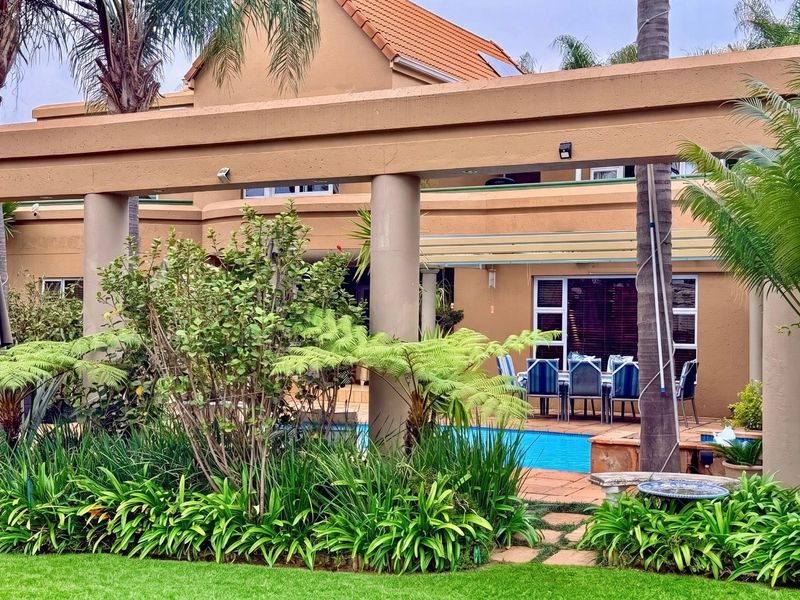 Rear view of the property featuring a swimming pool, paved patio area, and a pergola structure set within a landscaped garden.