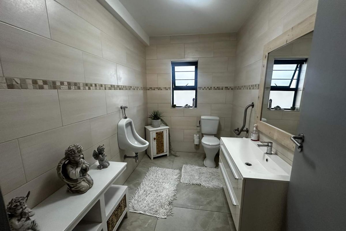 A spacious bathroom featuring neutral wall tiling, a modern vanity with integrated basin, a toilet, and a wall-mounted urinal.
