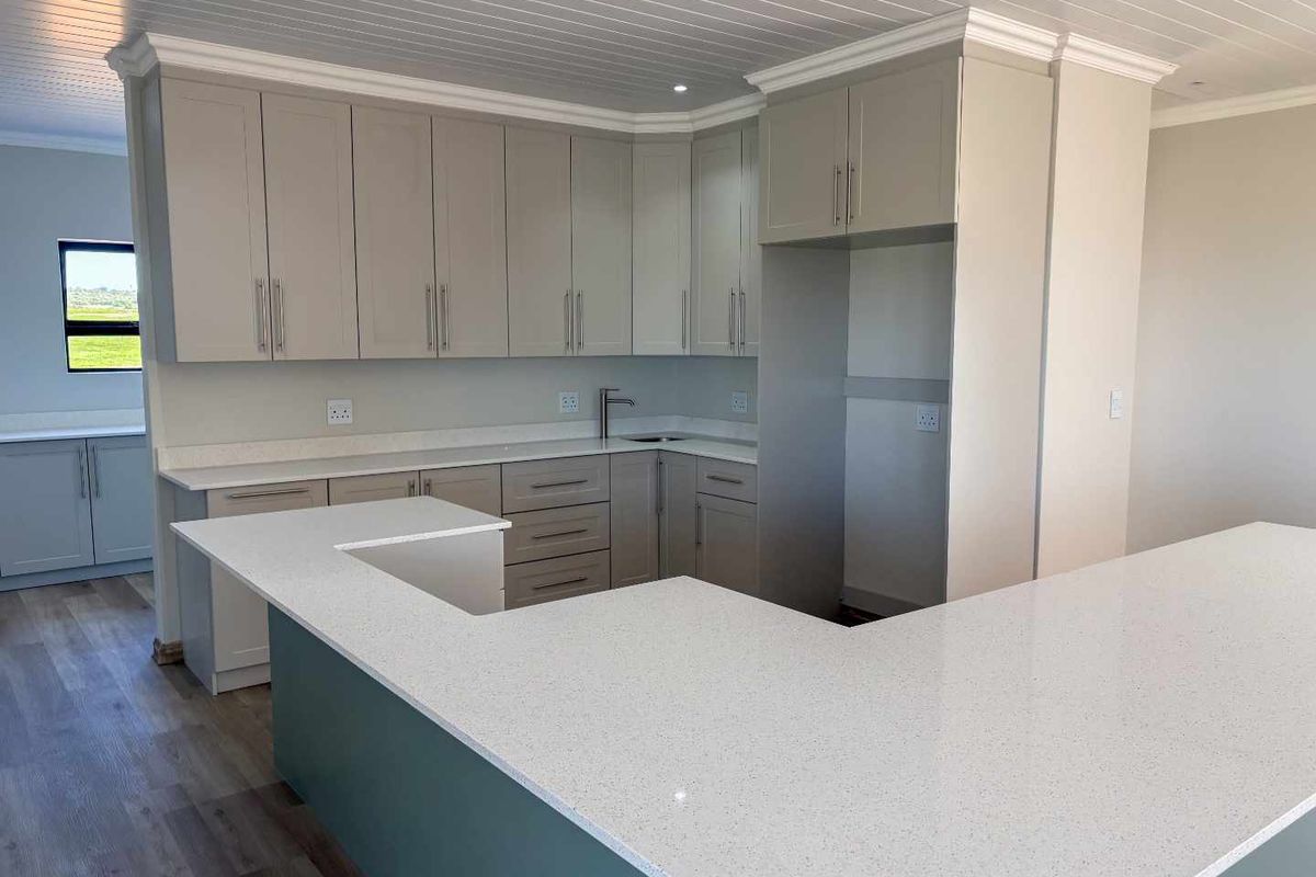 Modern kitchen featuring light grey cabinetry, stone countertops, a breakfast bar, and recessed ceiling lighting in an open-plan layout.