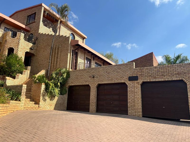 A multi-level brick residence featuring a triple garage, paved driveway, and elevated balconies with wrought iron railings.