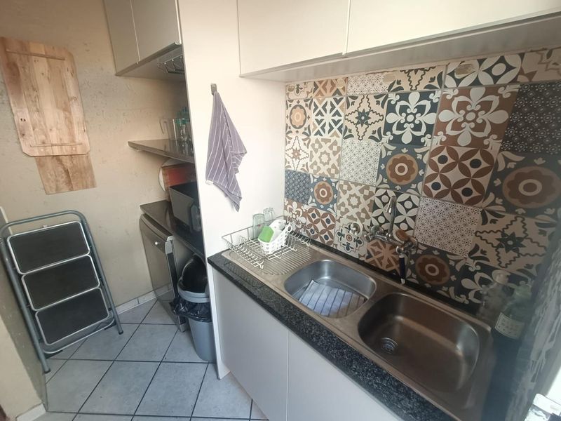 A functional scullery area featuring a double bowl stainless steel sink, patterned tile splashback, and built-in cabinetry with stone countertops.