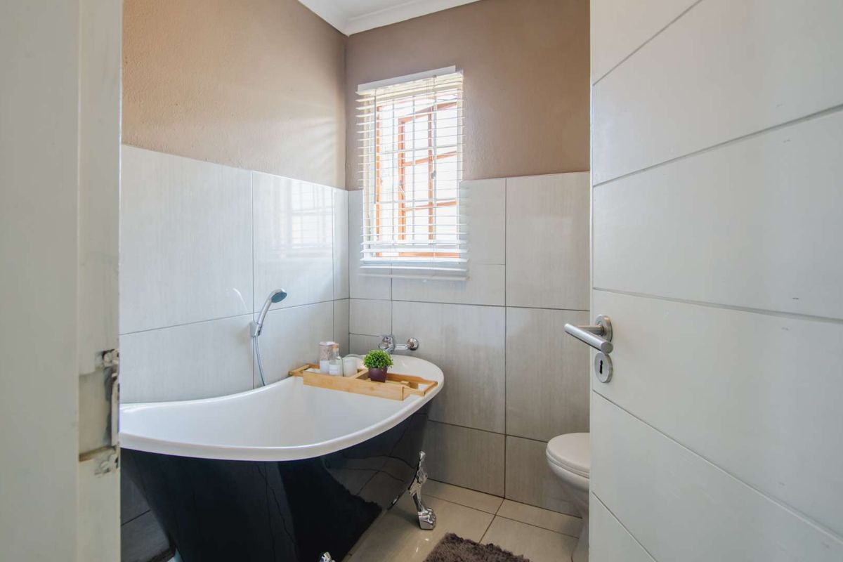 A modern bathroom featuring a freestanding black clawfoot bathtub with chrome fixtures, tiled walls, and a white toilet.