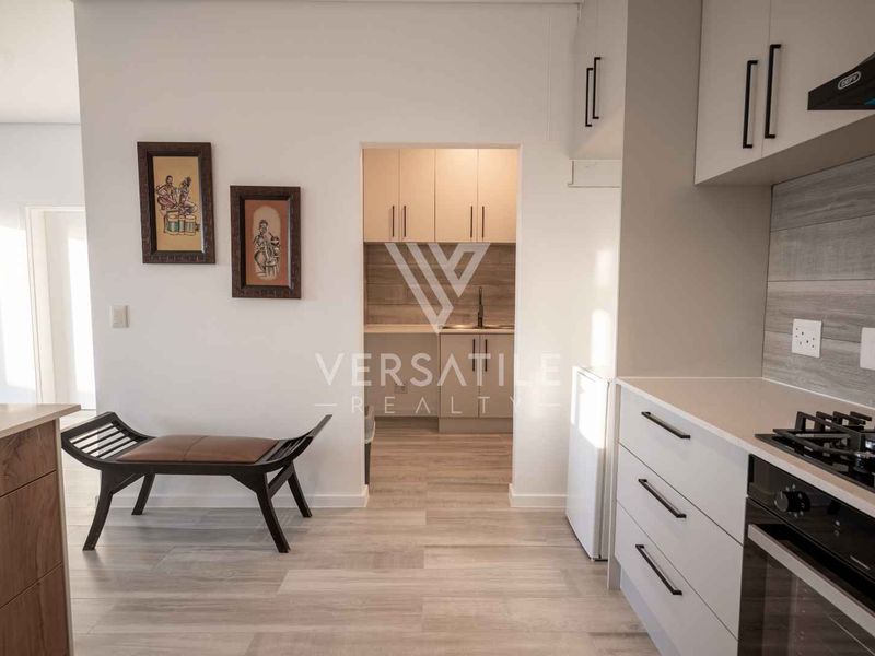 Modern open-plan kitchen featuring sleek white cabinetry, integrated appliances, and a separate scullery area with matching finishes and wood-look laminate flooring.