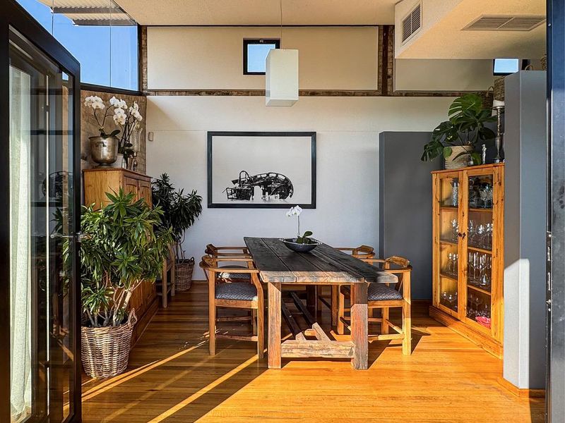 A bright dining room featuring warm hardwood flooring, high ceilings with clerestory windows, and integrated air conditioning, opening directly to an outdoor space.