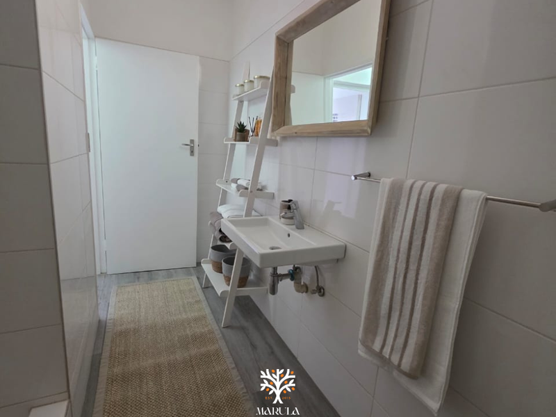 A clean and modern bathroom featuring a wall-mounted basin, chrome fixtures, and neutral wall tiling.