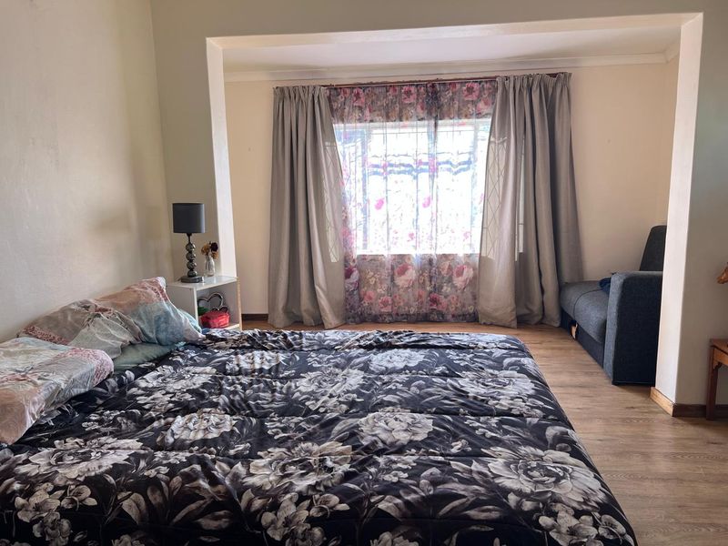 A spacious bedroom featuring laminate flooring, coving, and a large window with security bars, offering a functional and well-lit living space.