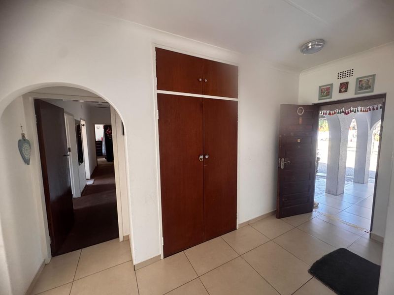 Entrance hall featuring tiled flooring, a built-in wooden cupboard, and an arched doorway leading to the interior hallway.