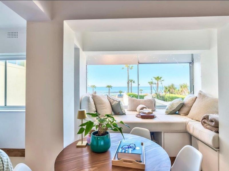 A bright living area featuring a custom built-in window seat with expansive ocean and palm tree views.