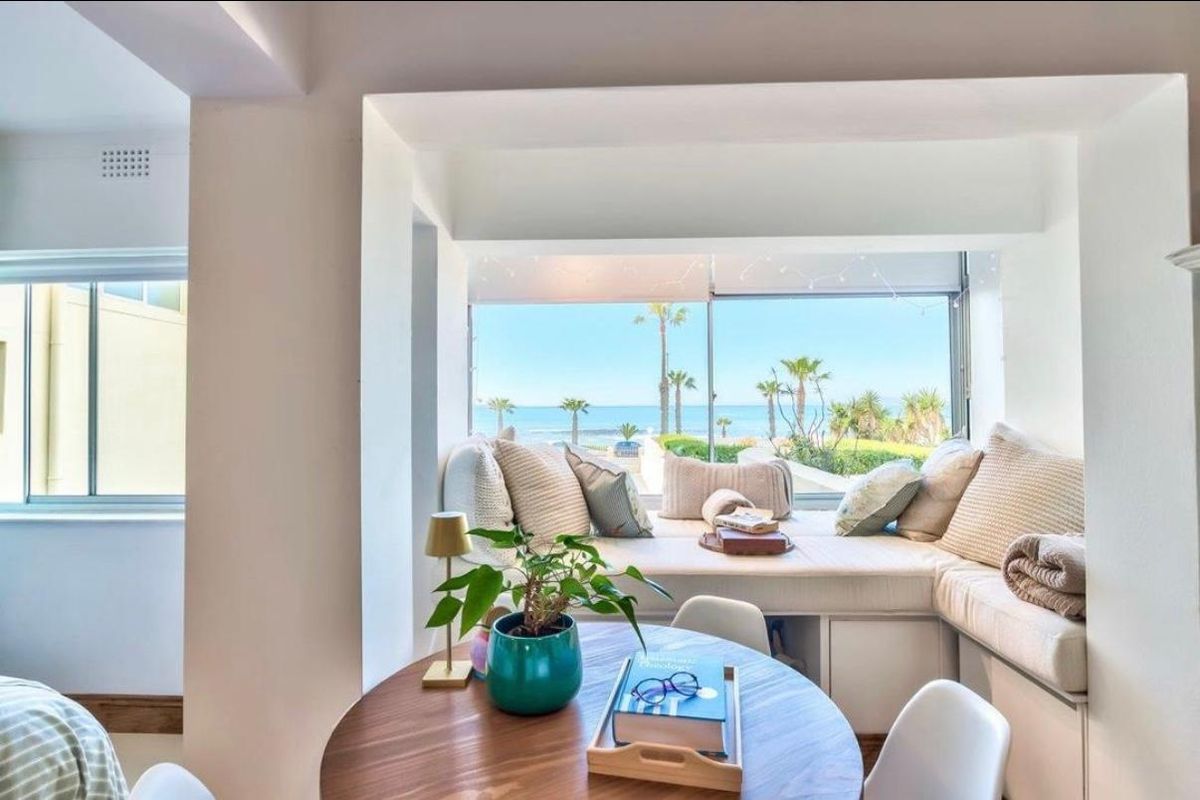 A bright living area featuring a custom built-in window seat with expansive ocean and palm tree views.