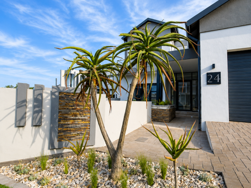 Modern front facade featuring a paved driveway, stone-clad feature wall, and well-maintained landscaped rock garden with architectural plants.