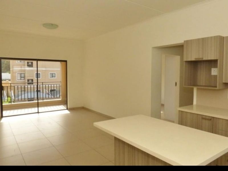 An open-plan living and kitchen area featuring modern cabinetry, a central island, tiled floors, and a sliding door leading to a balcony.