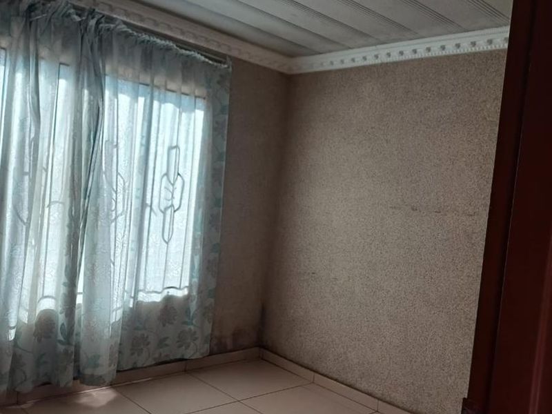 An empty bedroom featuring tiled flooring, ceiling moulding, and a flush mount light fixture, showing signs of wall dampness and wear.