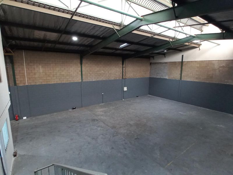 Spacious industrial warehouse area featuring high ceilings, exposed steel trusses, concrete flooring, and large skylights providing ample natural light.