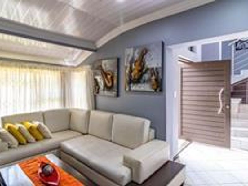 A bright living room featuring vaulted ceilings, tiled flooring, and an open transition to the entrance hall with a modern staircase.