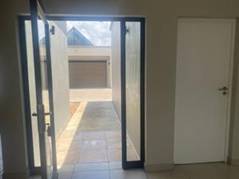 An interior view of an entrance area featuring tiled flooring and a glass door leading to an exterior courtyard and garage.