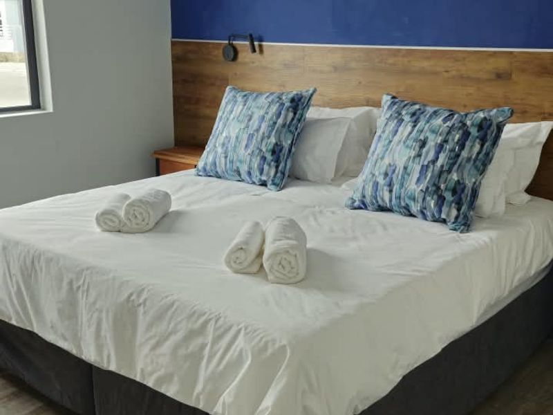 A well-maintained bedroom featuring wood-look laminate flooring, a decorative blue accent wall, and a built-in timber-look headboard with integrated lighting.