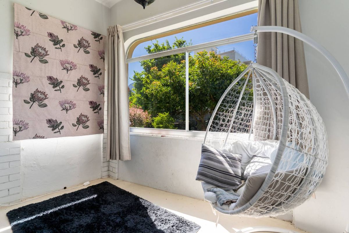 A bright bedroom featuring a large window with garden views, white painted brick walls, and neutral curtains.