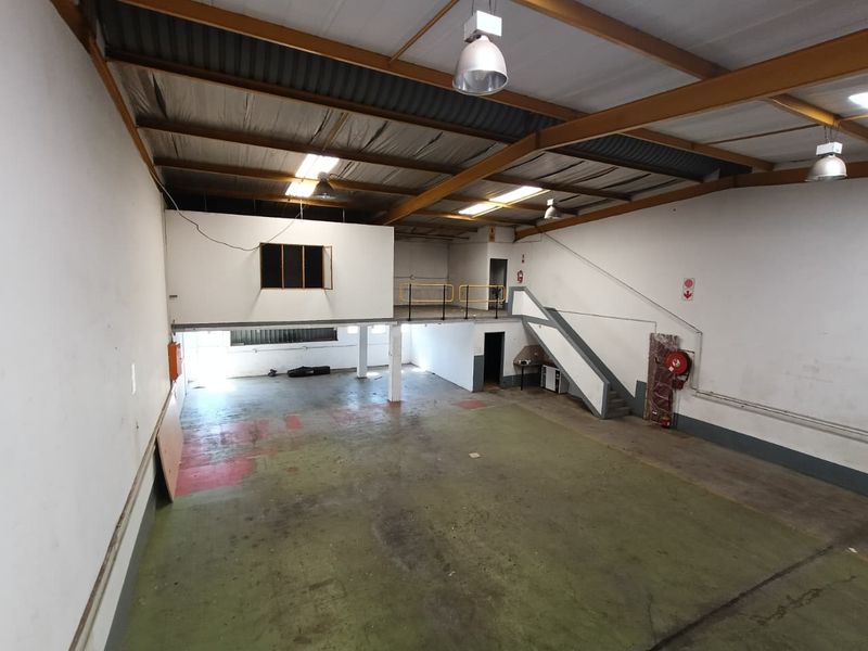 Spacious industrial warehouse unit featuring a mezzanine level, high ceilings with exposed steel trusses, concrete flooring, and an internal staircase.
