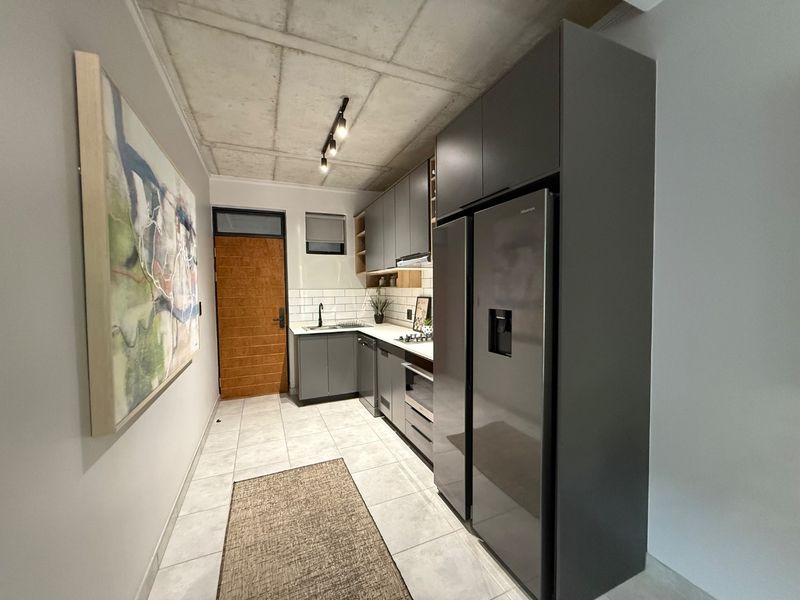 Modern kitchen featuring sleek grey cabinetry, subway tile backsplash, exposed concrete ceiling, and high-quality built-in appliances in a contemporary apartment setting.