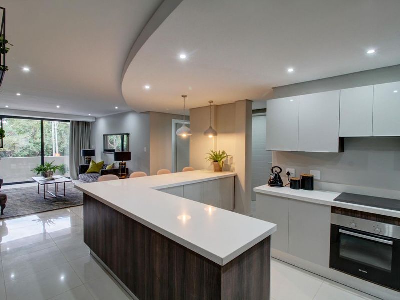 Modern open-plan kitchen and living area featuring sleek cabinetry, quartz countertops, integrated appliances, and large sliding doors leading to a balcony.