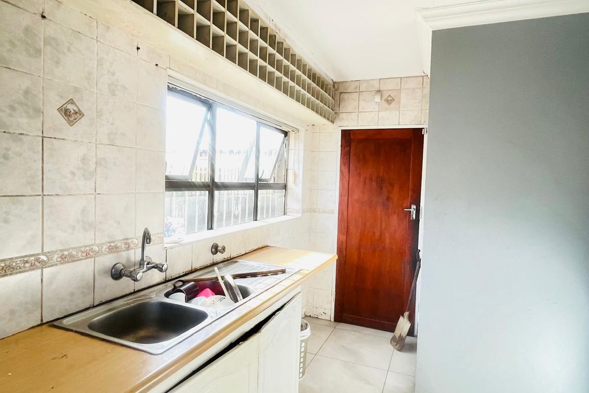 A functional kitchen area featuring a double stainless steel sink, tiled splashbacks, and wooden cabinetry, providing a practical workspace for office staff.