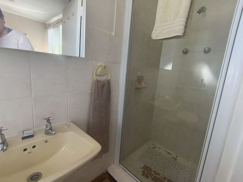 A functional bathroom featuring a shower enclosure with tiled flooring and a wall-mounted basin, showing signs of age and wear in the finishes.
