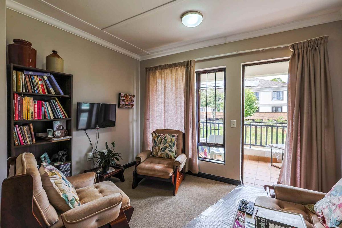 A cozy living room featuring carpeted flooring, a ceiling-mounted light fixture, and direct access to a private balcony through a glass door.