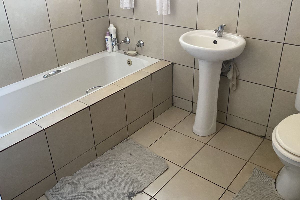 A functional bathroom featuring a built-in bathtub, pedestal basin, and toilet with neutral wall and floor tiling.