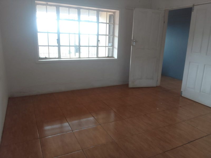 An empty bedroom featuring tiled flooring, a multi-pane window, and white panel doors, offering a blank canvas for potential renovation or interior design.