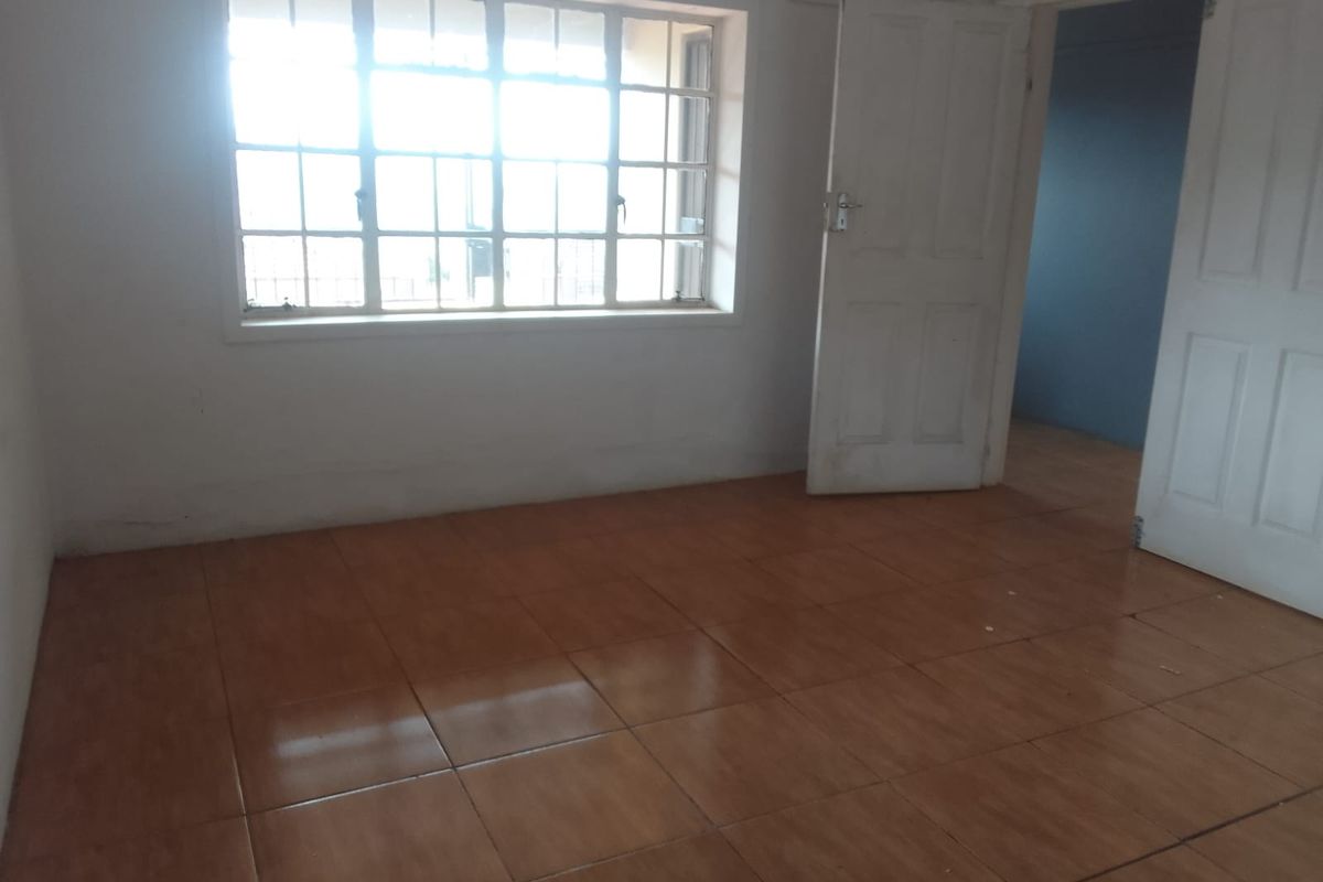 An empty bedroom featuring tiled flooring, a multi-pane window, and white panel doors, offering a blank canvas for potential renovation or interior design.