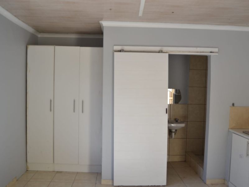 A bedroom featuring built-in cupboards and a sliding door leading to an en-suite bathroom, with tiled flooring and neutral wall finishes.