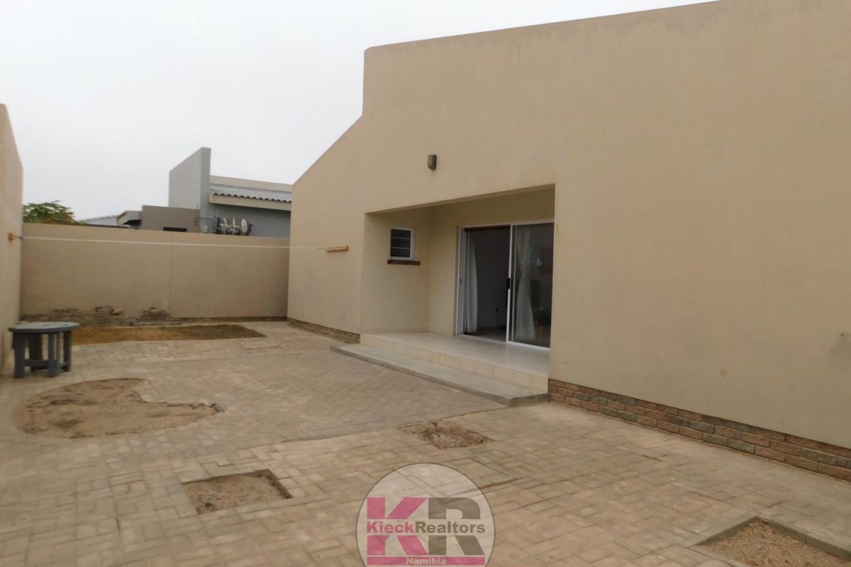 Rear exterior view of the property featuring a paved courtyard, boundary wall, and sliding door access to the interior living space.