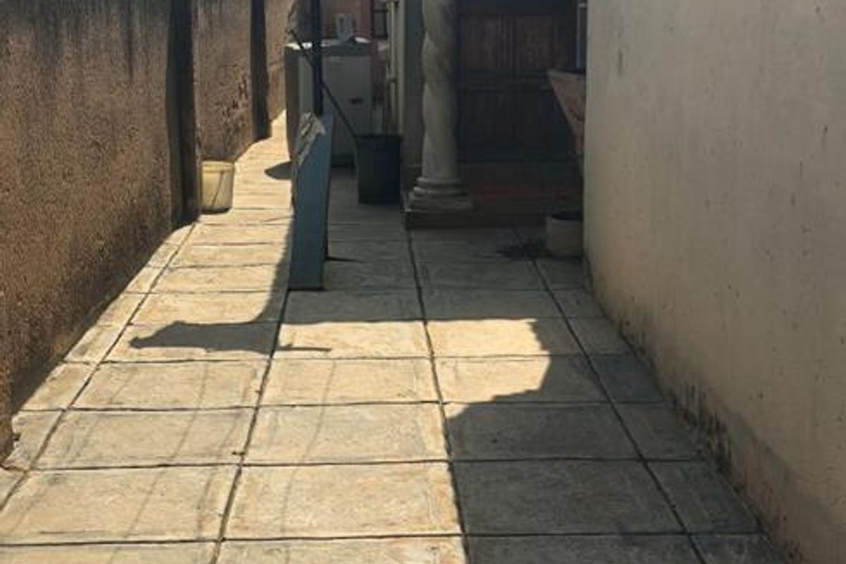 A narrow side exterior walkway featuring paved flooring and a decorative column leading to a rear entrance.