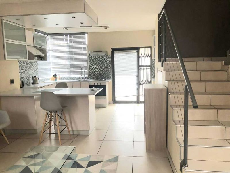 Open-plan living area featuring a modern kitchen with mosaic backsplash, built-in appliances, tiled flooring, and a staircase leading to the upper level.