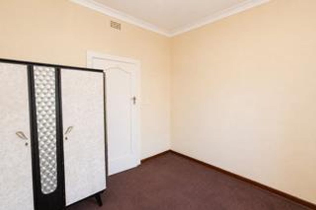 A simple bedroom featuring neutral wall paint, carpeted flooring, and a classic internal door with decorative molding.