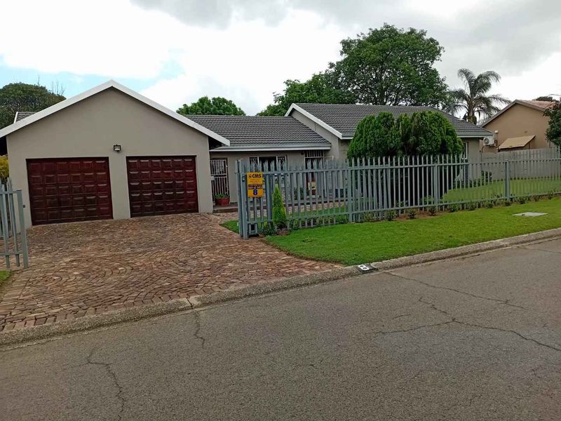Front view of a residential property featuring a double garage, paved driveway, and secure steel fencing with a well-maintained lawn.