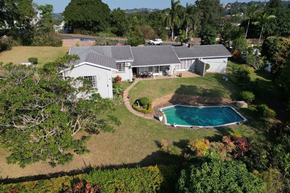 Aerial view of a residential property featuring a spacious garden, a swimming pool, a paved patio area, and a well-maintained tiled roof house.