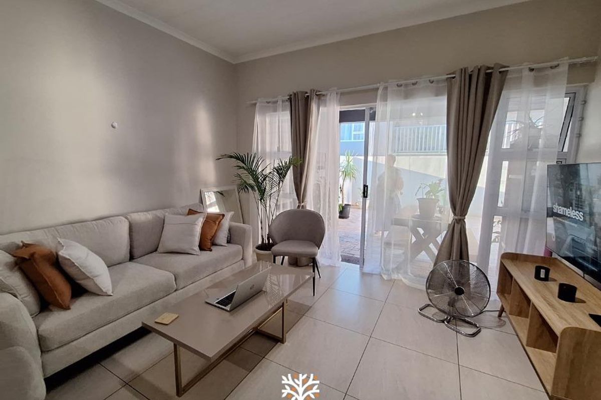 A bright and inviting living room featuring large sliding glass doors that open onto a private patio, finished with neutral floor tiles.