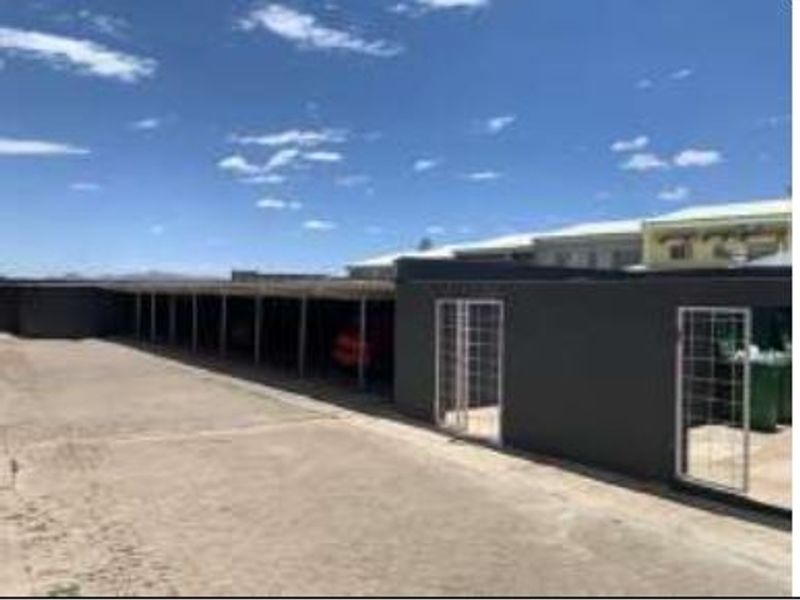 A row of covered parking bays with security gates and a paved driveway area.