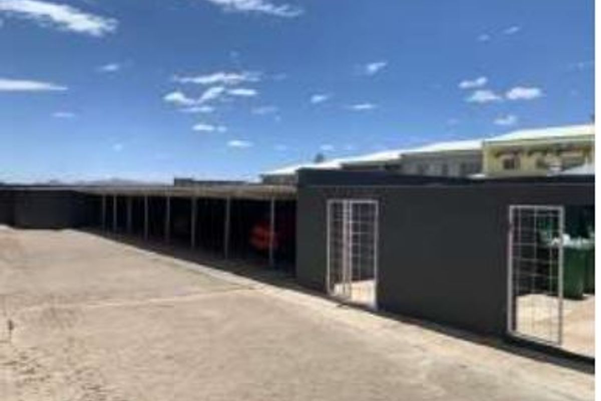 A row of covered parking bays with security gates and a paved driveway area.