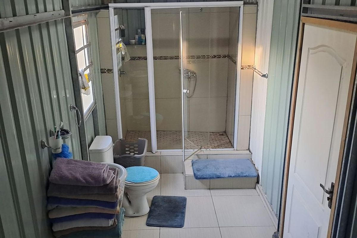 A functional bathroom featuring a shower enclosure, toilet, and tiled flooring, finished with industrial-style corrugated metal wall cladding.