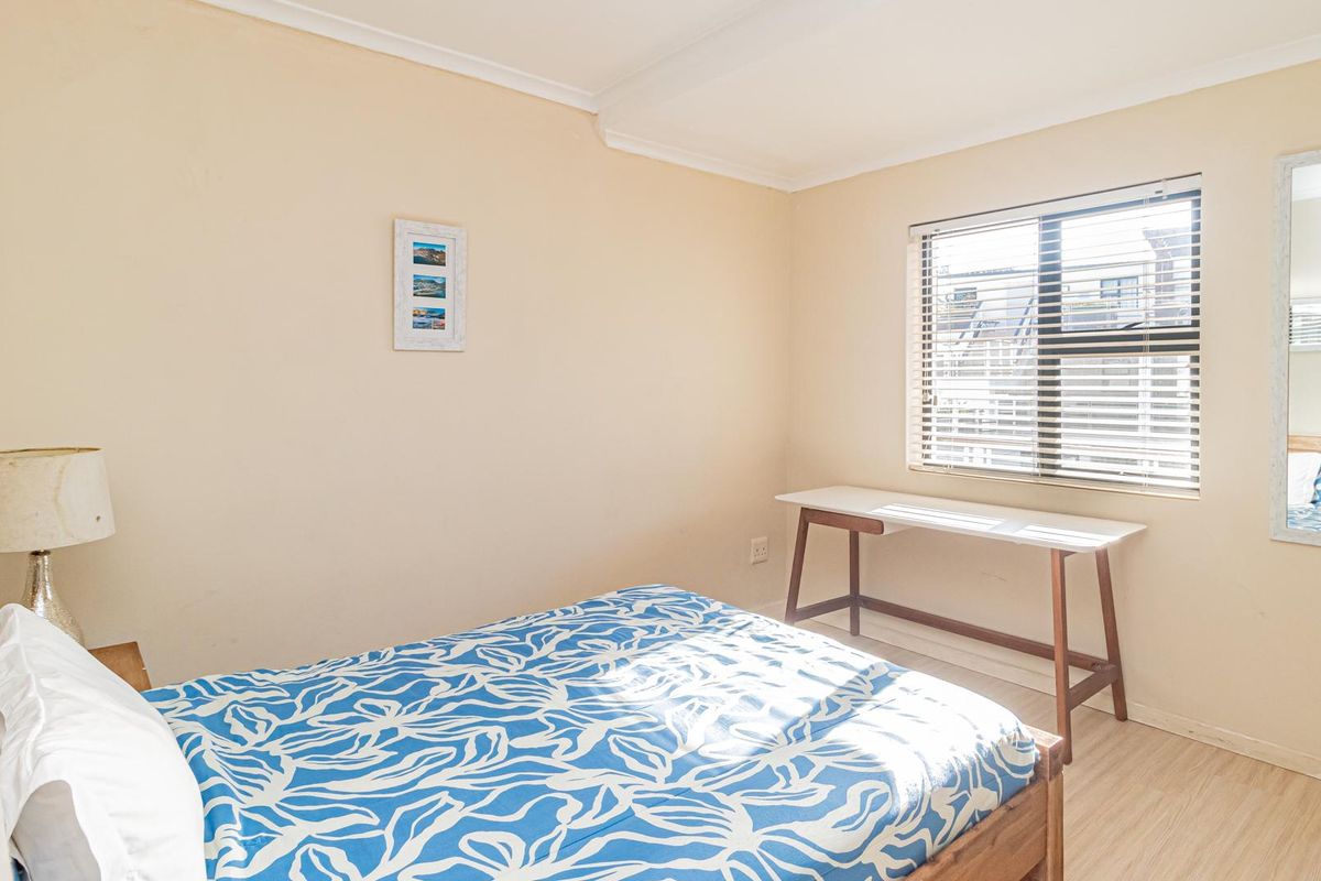A functional bedroom featuring laminate flooring, neutral wall tones, and a window fitted with venetian blinds.
