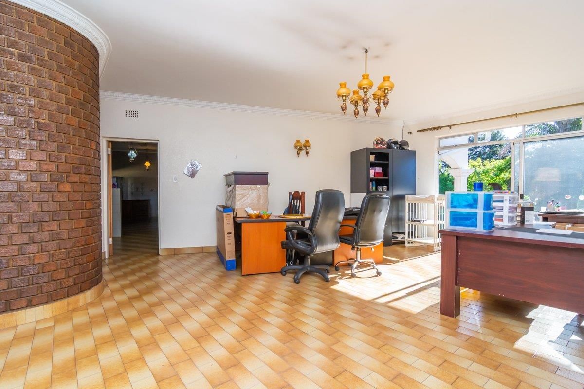A spacious living area featuring a distinctive curved brick feature wall, tiled flooring, and large windows providing natural light.