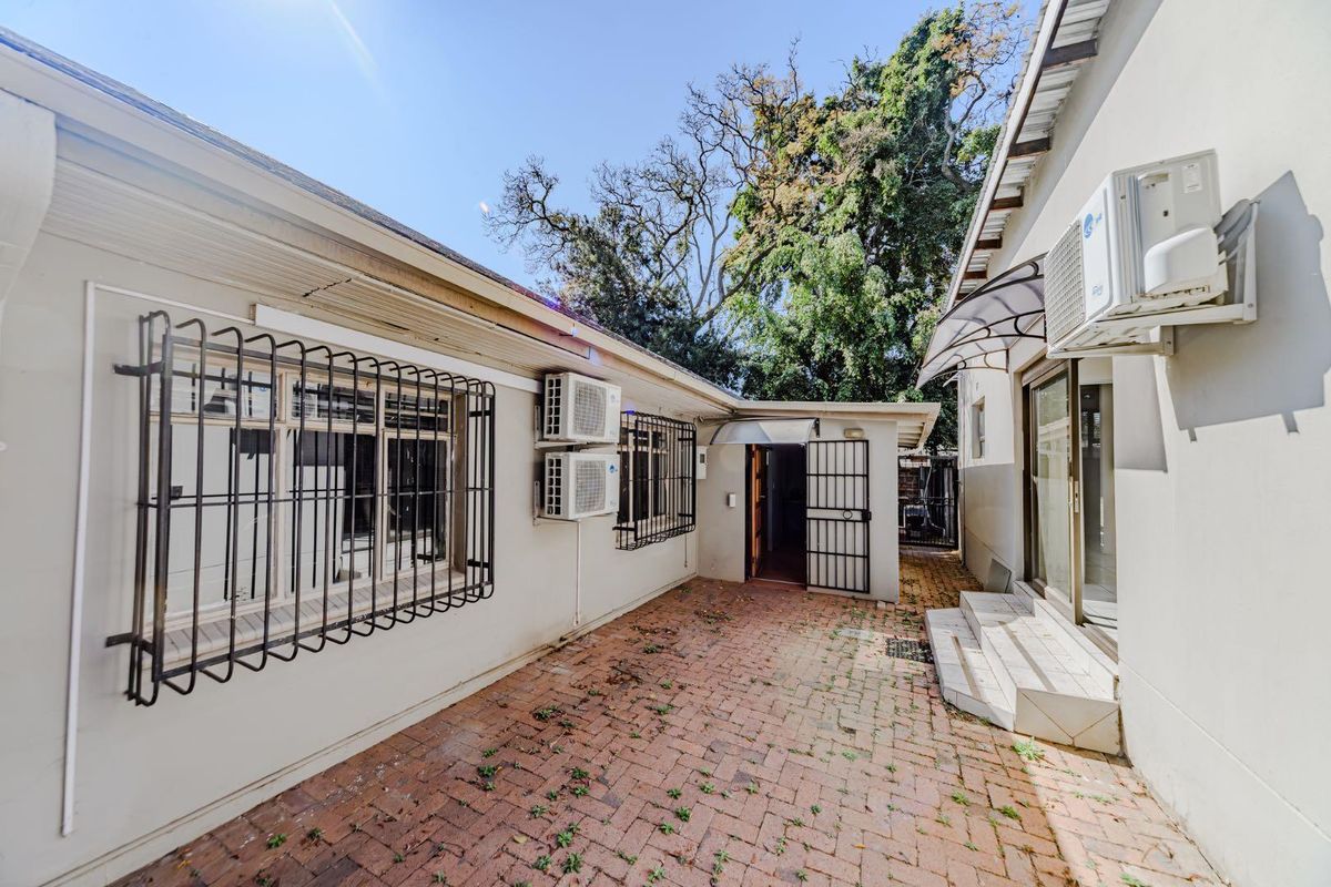 Rear courtyard area featuring brick paving, security bars on windows, and wall-mounted air conditioning units.