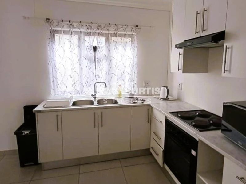A functional kitchen featuring white built-in cabinetry, a double sink, integrated electric hob, oven, and extractor fan with tiled flooring.