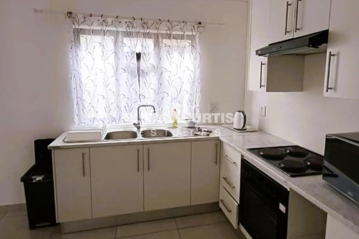 A functional kitchen featuring white built-in cabinetry, a double sink, integrated electric hob, oven, and extractor fan with tiled flooring.